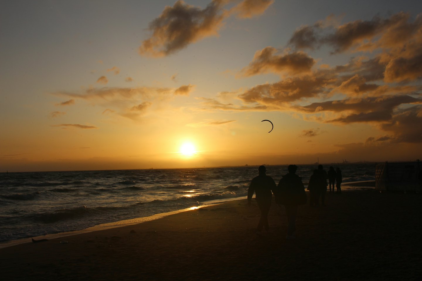 People walk along a sandy beach at sunset.